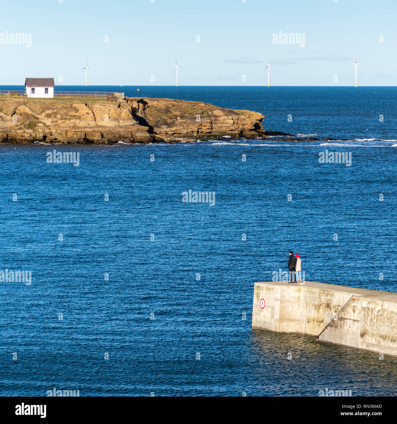 Tynemouth, England, UK - February 4, 2019: A couple walk along the breakwater of Cullercoats Harbour on the North Sea coast of Tyneside. Stock Photo