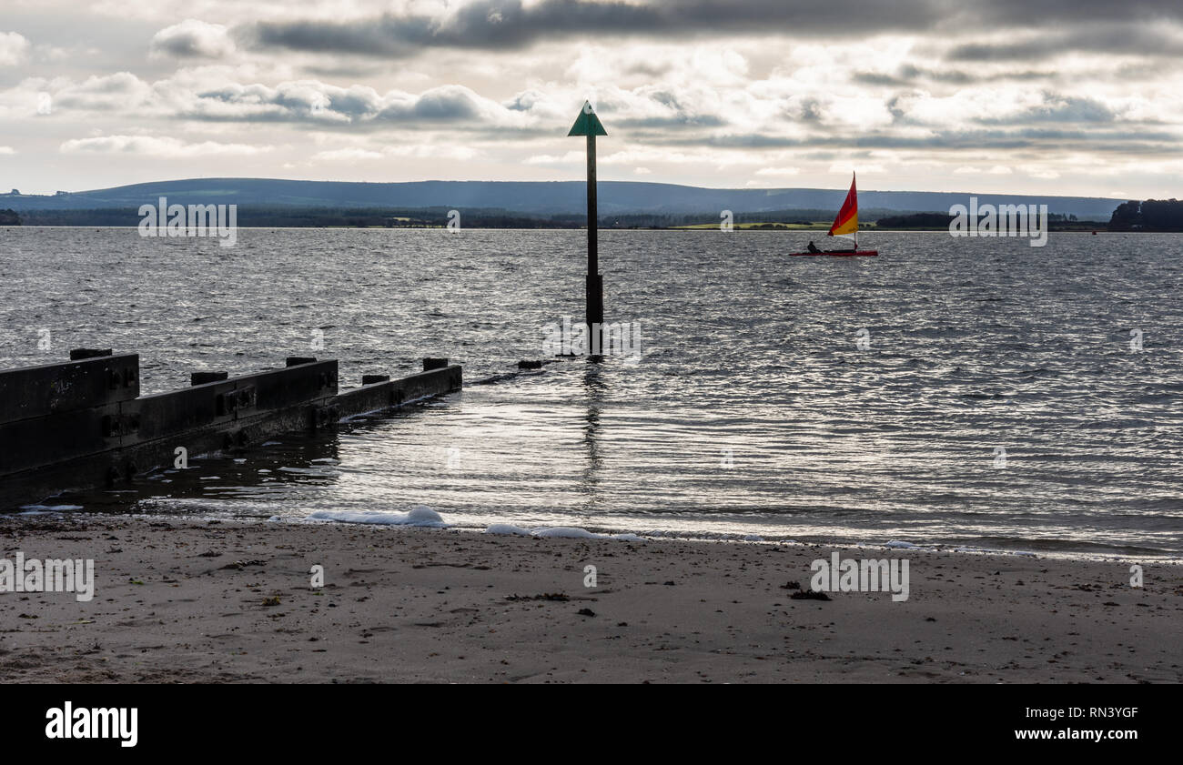 Poole, England, UK - December 26, 2018: A man sails a dinghy at Hamworthy in Poole Harbour, with the Purbeck Hills in the background. Stock Photo