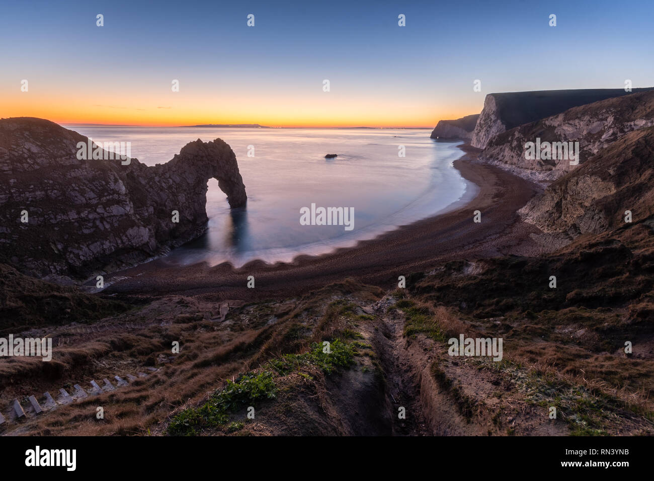 The afterglow of sunset lights up the sky behind Durdle Door and Bat's Head on Dorset's Jurassic Coast. Stock Photo