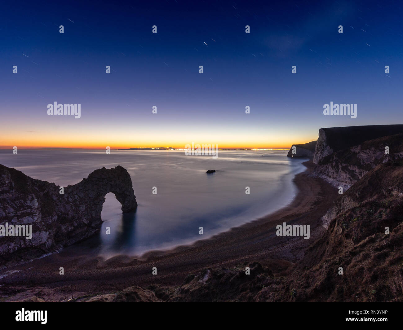 Stars become visible in the night sky above the final afterglow of sunset at Durdle Door and Bat's Head on Dorset's Jurassic Coast. Stock Photo