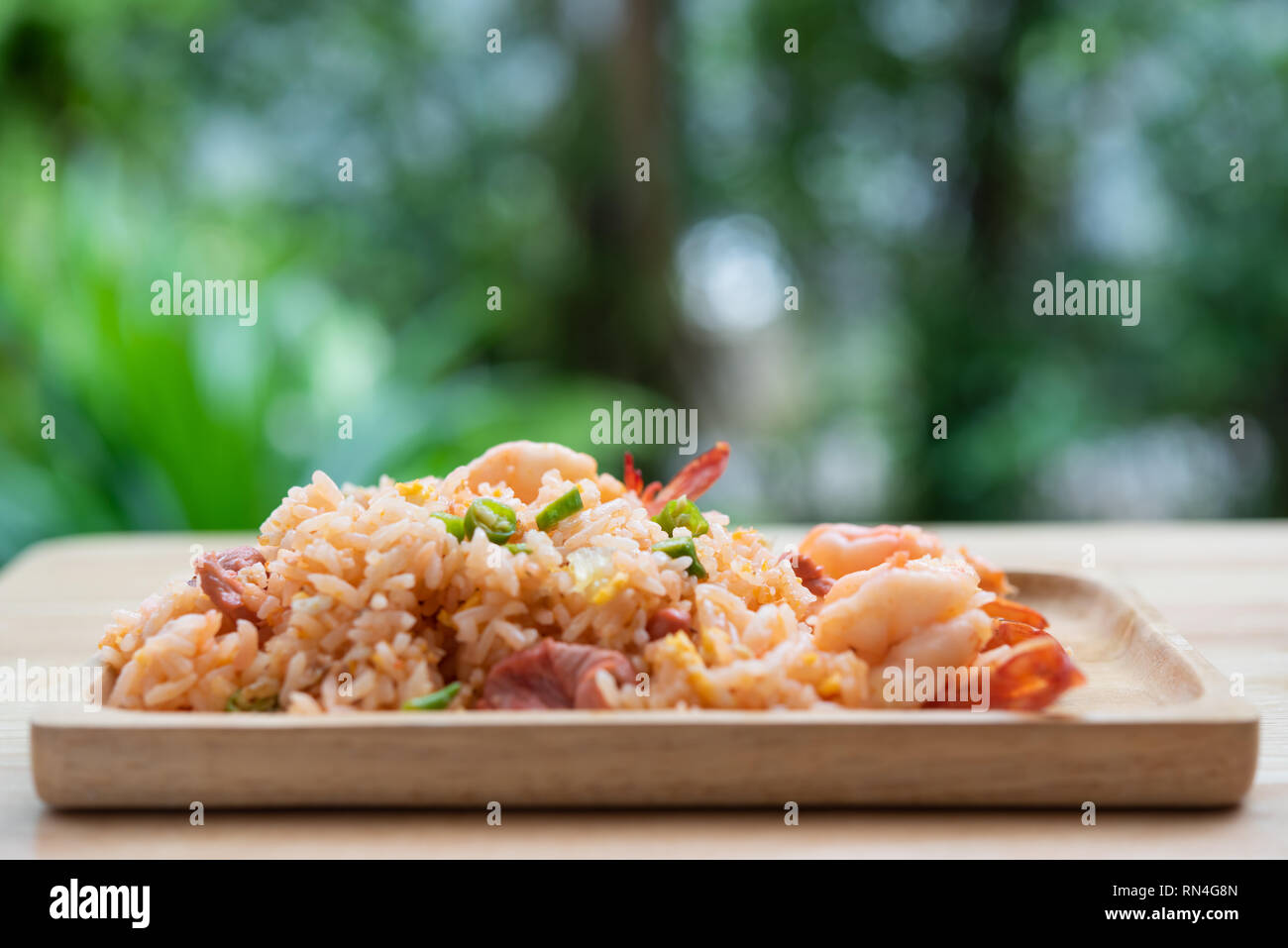 Delicious Thai fried rice with shrimp on wooden table with beauitful vase ,green blurred background Stock Photo