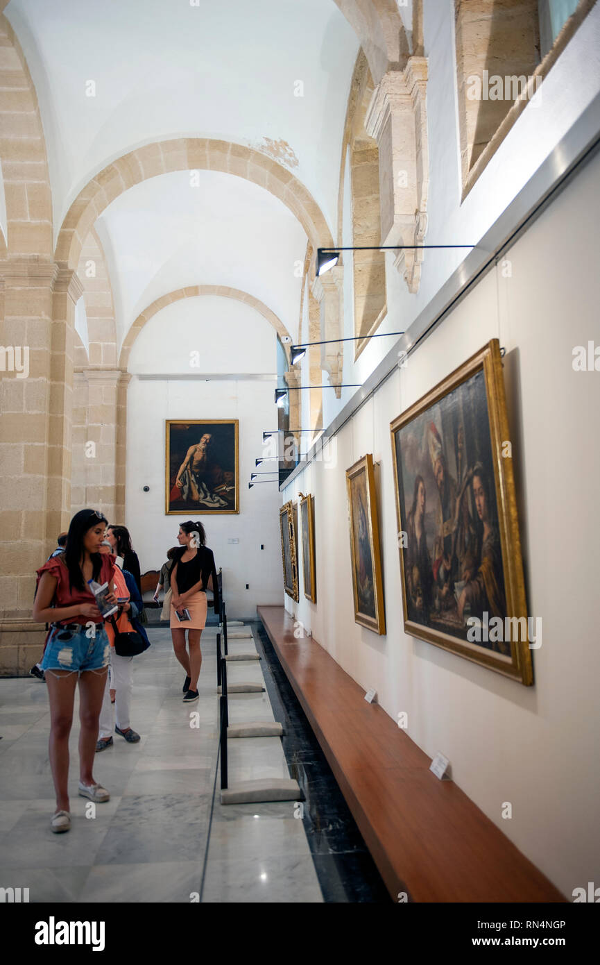 Tourists look at paintings from Seville's 17th century Golden Age in the Sala del Pabellon of Seville Cathedral. Built on the site of the Moorish 12th Stock Photo