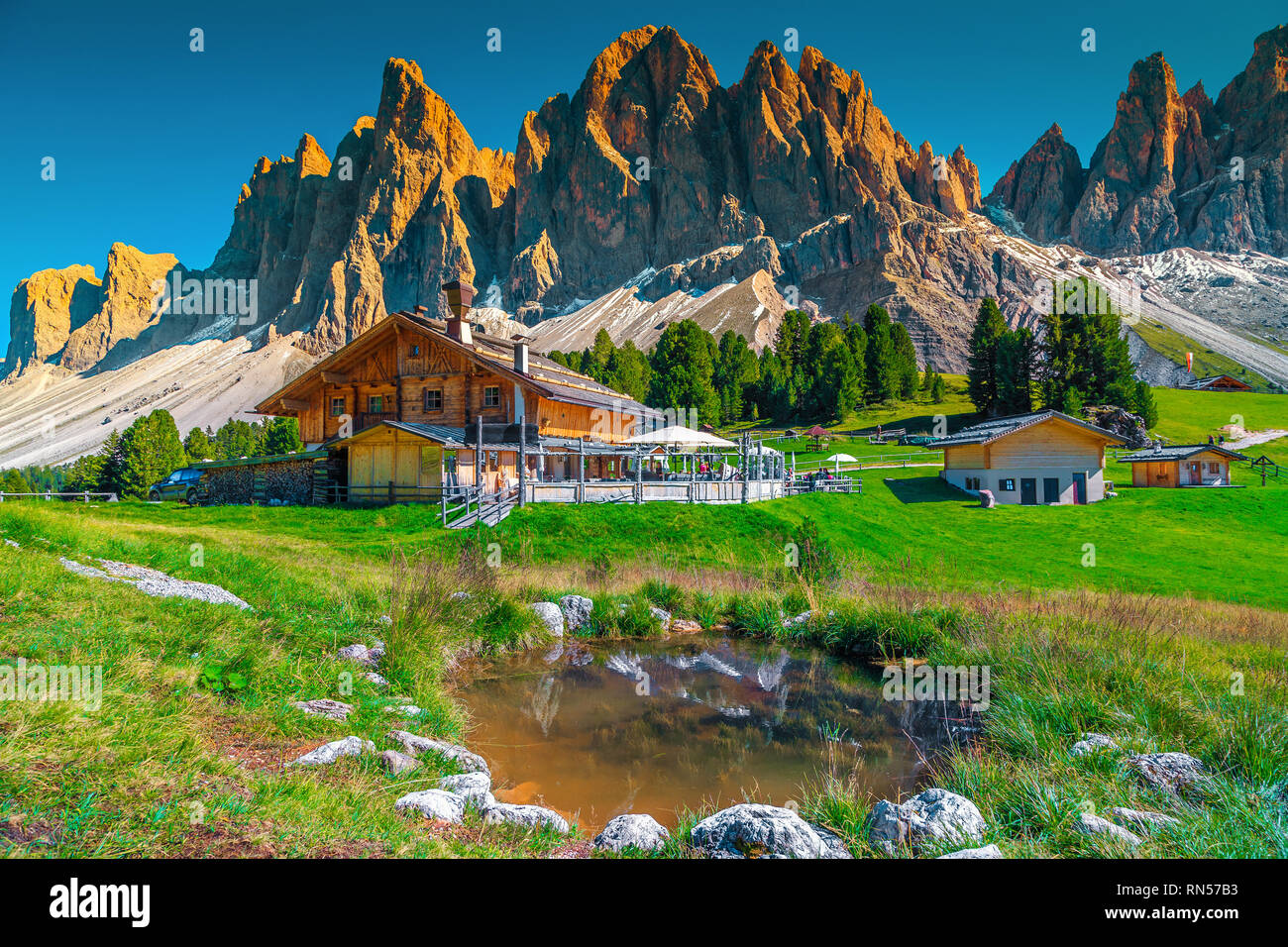 Beautiful spring alpine landscape, mountain chalets and small lake with high snowy mountains in background at sunset, Geisler - Odle mountain group, A Stock Photo