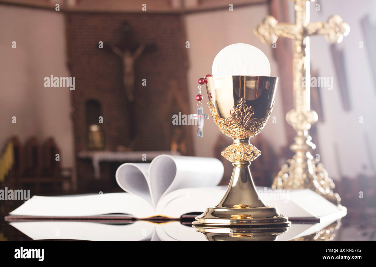 The Cross, golden chalice, rosary and Bible on the wooden altar. Stock Photo