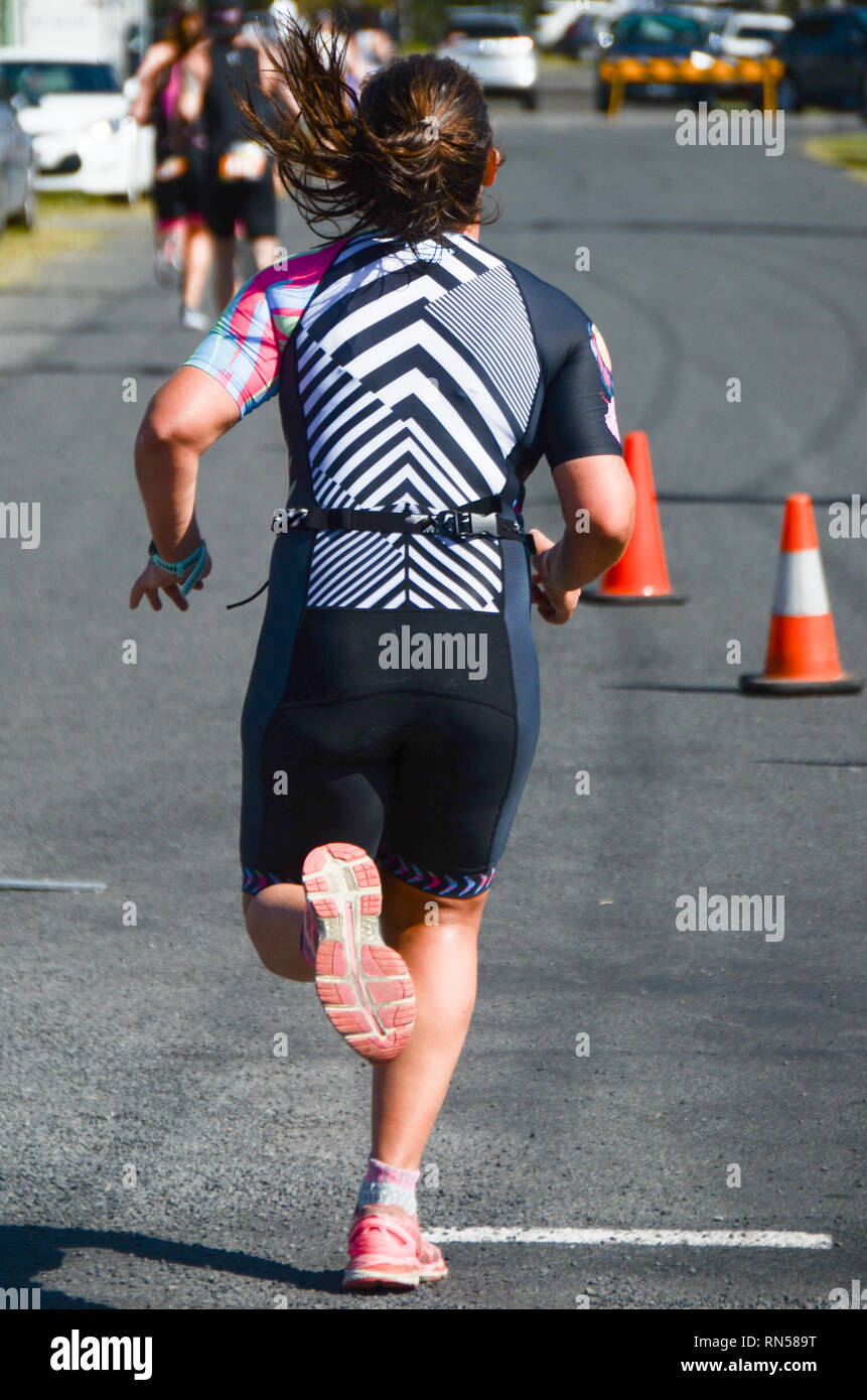 Female  athletic competitor running during endurance road race. Sportswoman runs outdoors on urban street. Stock Photo