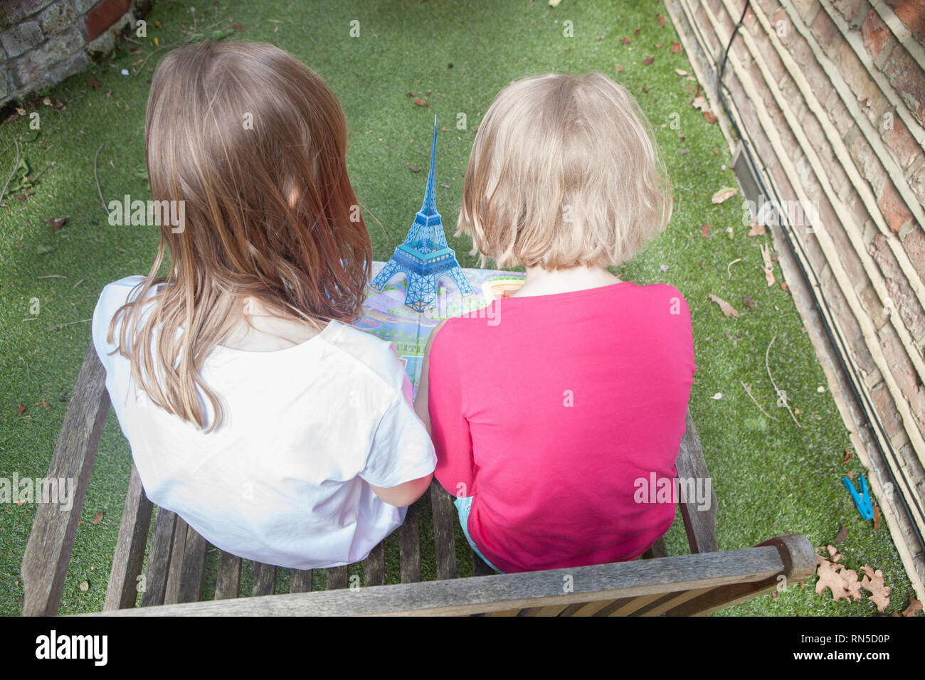 two young girls reading a pop up book on Paris in their garden Stock Photo