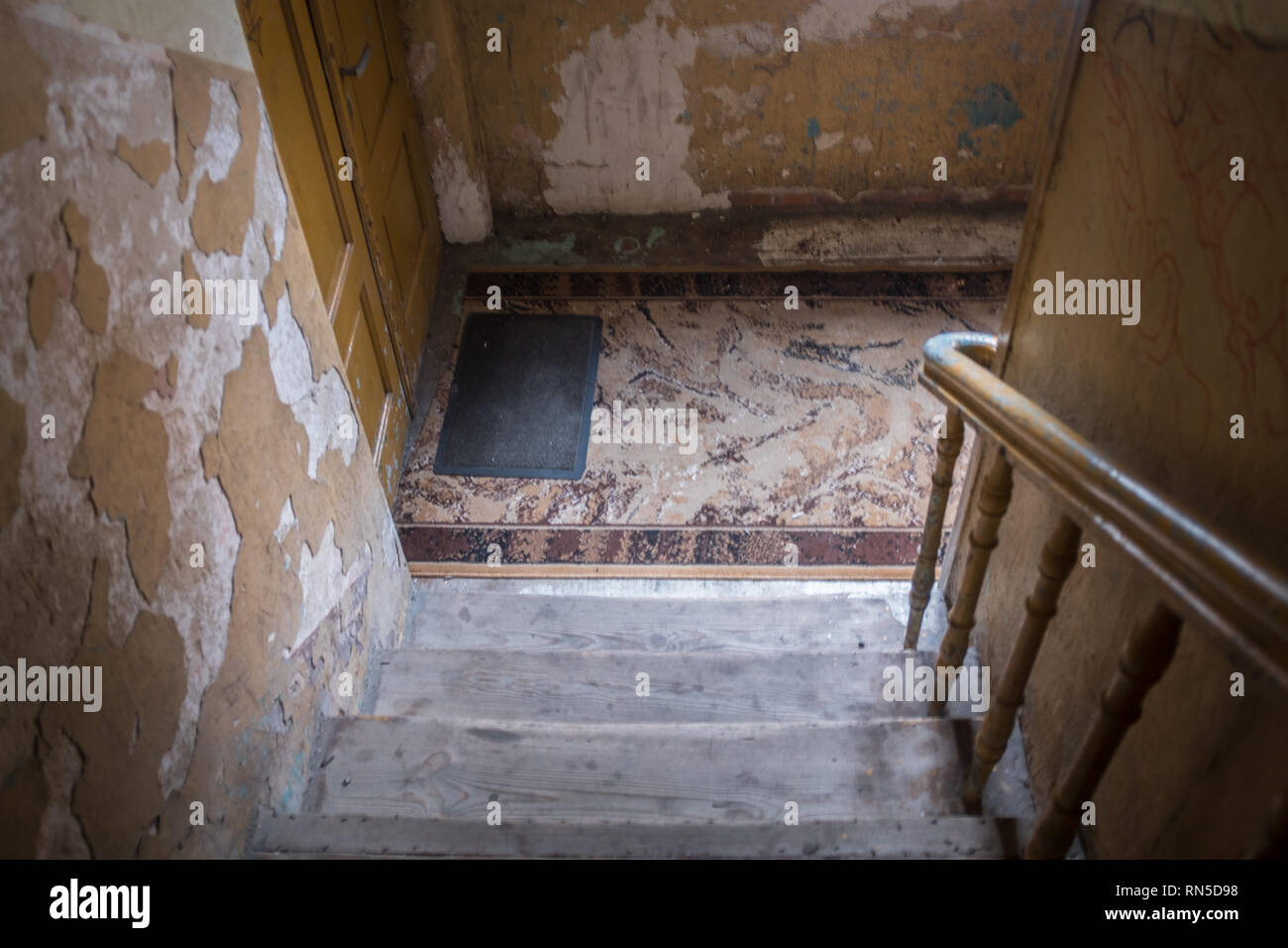 Interior of tatty tenement block hallway with staircase leading to front door Stock Photo