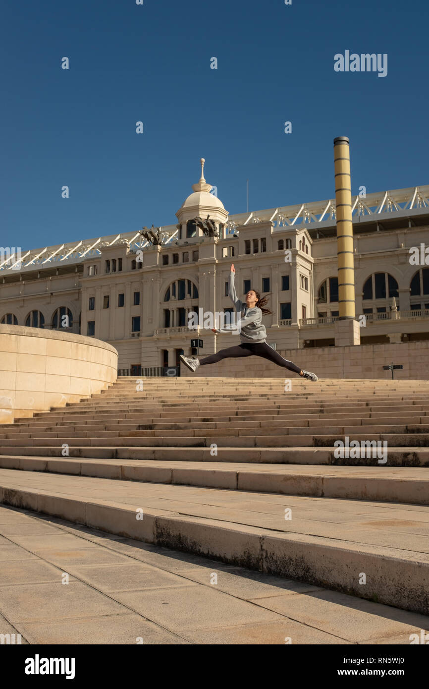 A young attractive girl makes a dance jumps leap along the staircase leading to the 'Estadi Olímpic Lluís Companys', Barcelona, Spain Stock Photo