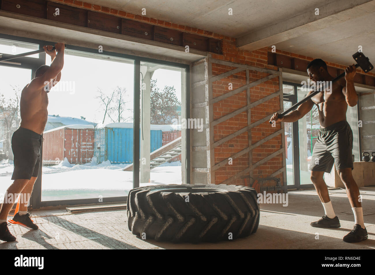 Two interracial sportsmen practicing Sledge hammer Hits, crossfit