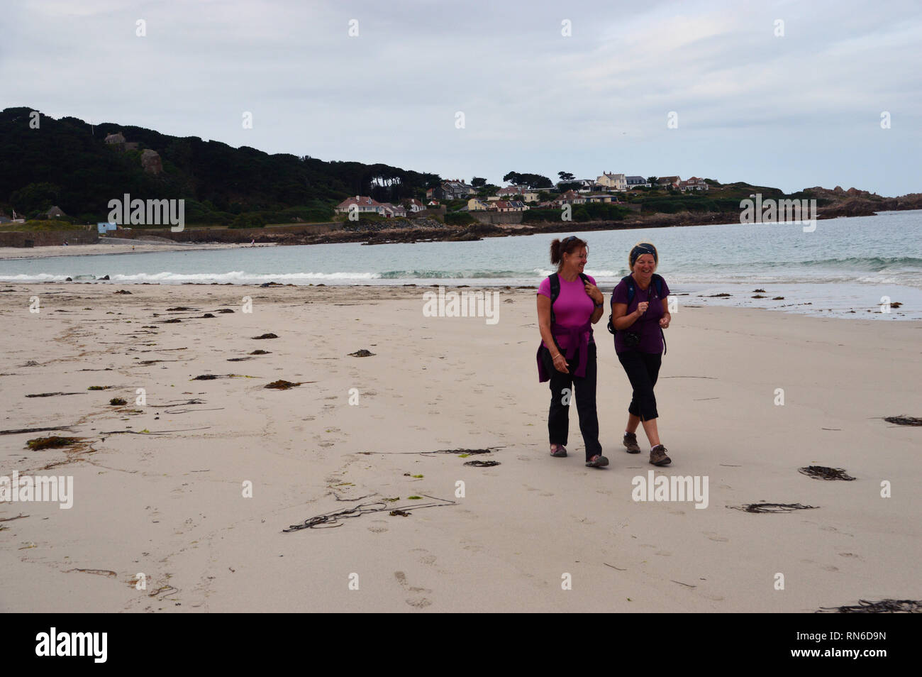 Two Women Hikers Walking, Talking & Laughing on Cobo Bay Beach Guernsey, Channel Islands. UK. Stock Photo