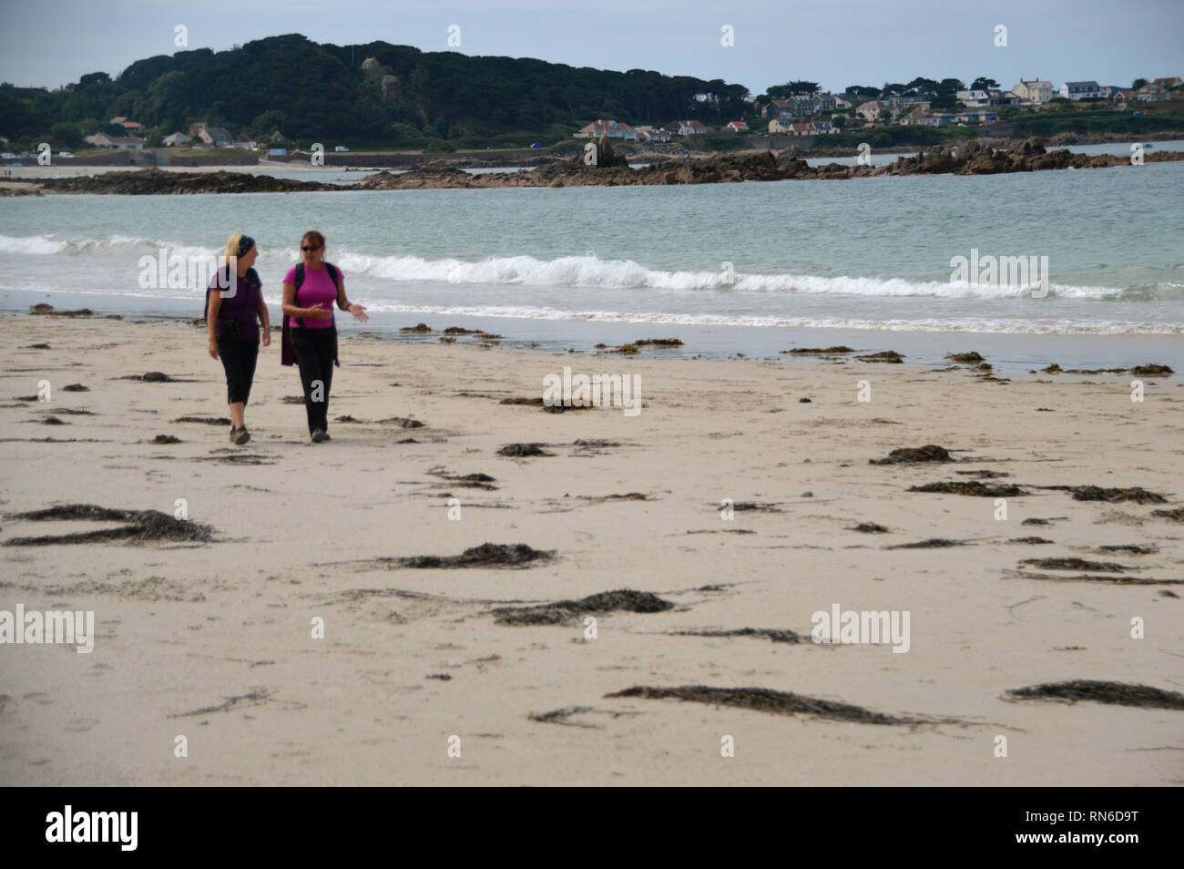 Two Women Hikers Walking, Talking & Laughing on Cobo Bay Beach Guernsey, Channel Islands. UK. Stock Photo