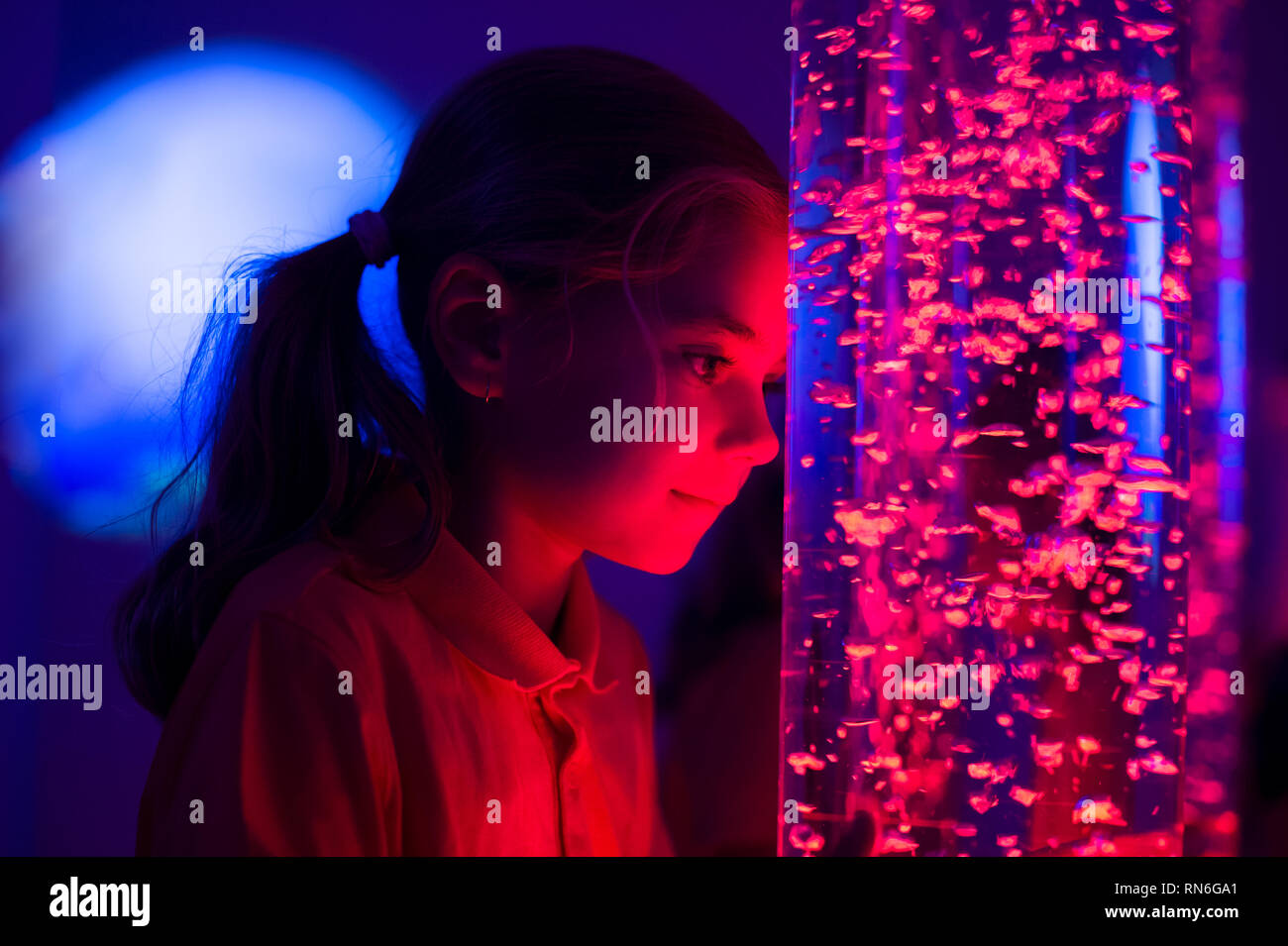 Child in therapy sensory stimulating room, snoezelen. Child interacting with colored lights bubble tube lamp during therapy session. Stock Photo