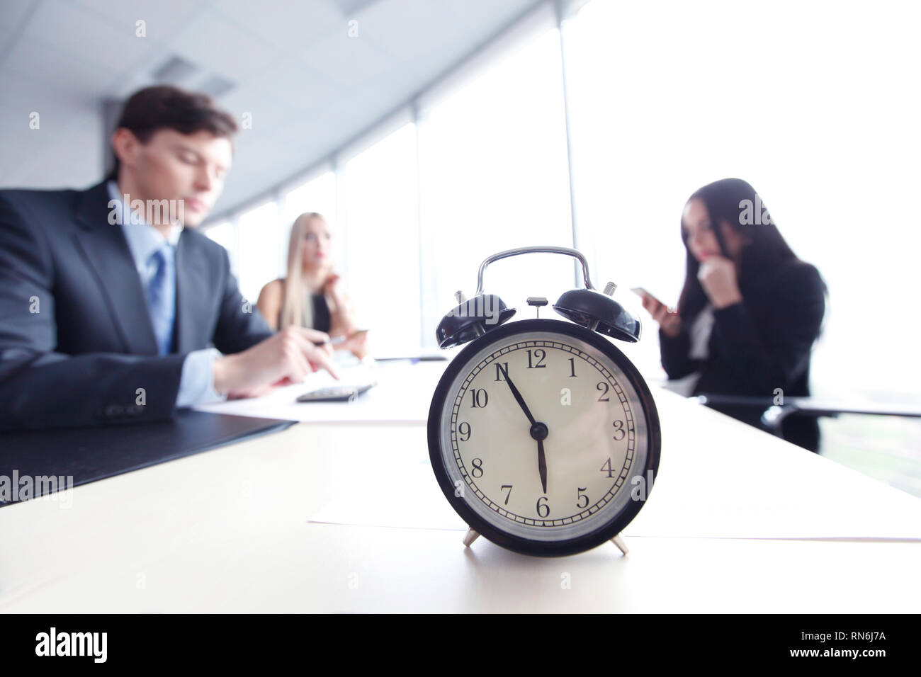 Alarm clock on office table with business discussion people group or