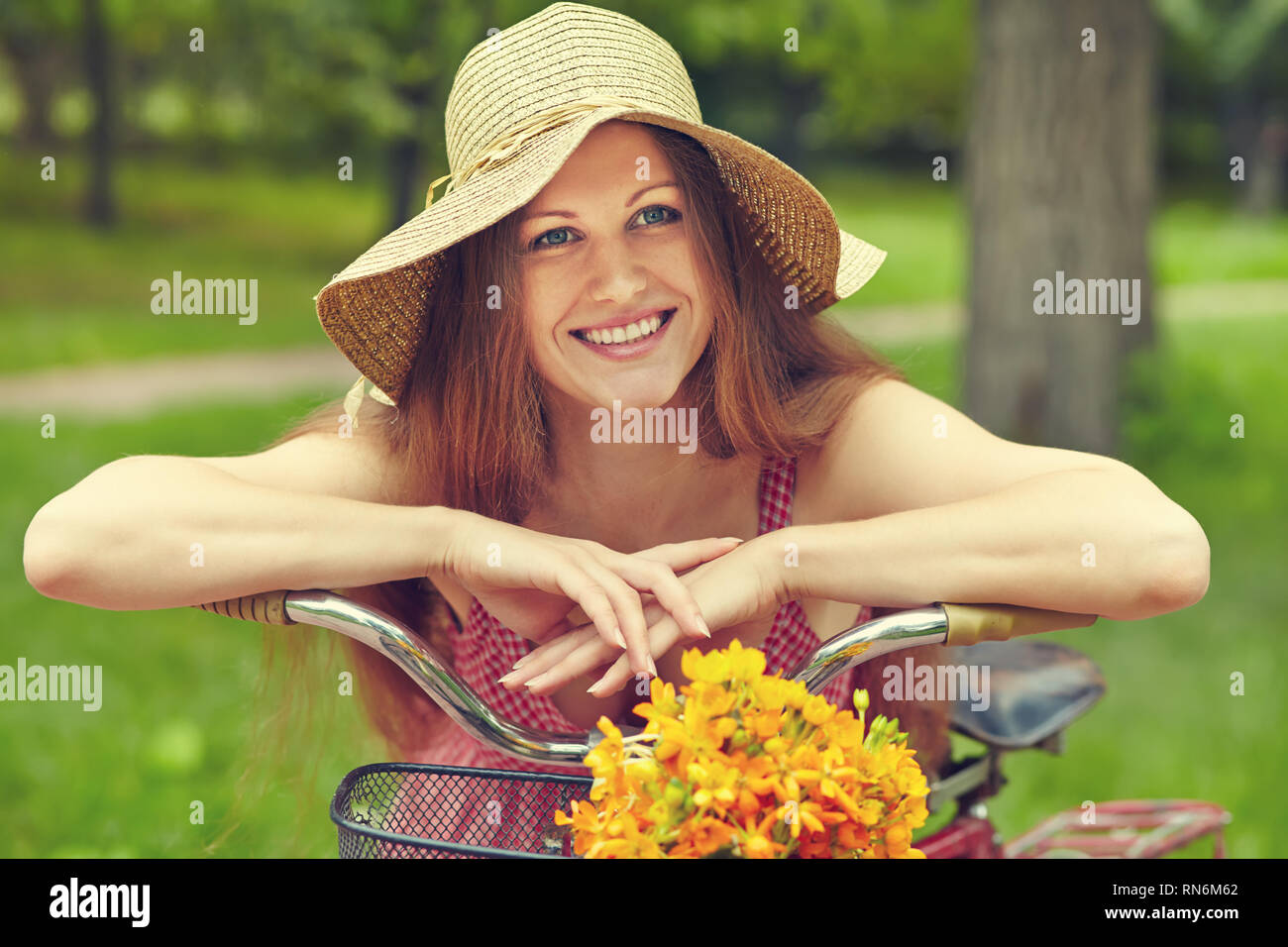 young woman in a dress and hat with a bike with flowers in a basket in a summer park Stock Photo