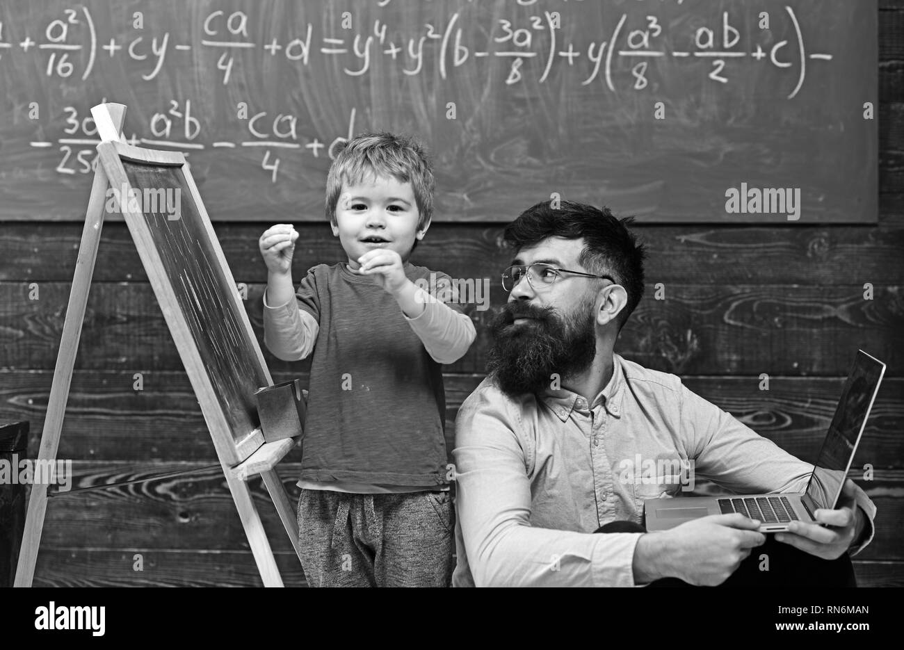 Kid reciting a poem while teacher listens attentively. Cool guy in pink shirt sitting on floor next to standing kid. Back to school Stock Photo