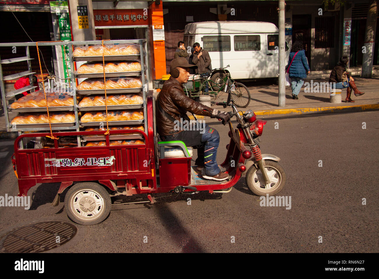 Chinese man riding a cargo moped loaded with bread from a baker in a street in China. Cargo bikes or freight mopeds are popular transport in China. Be Stock Photo