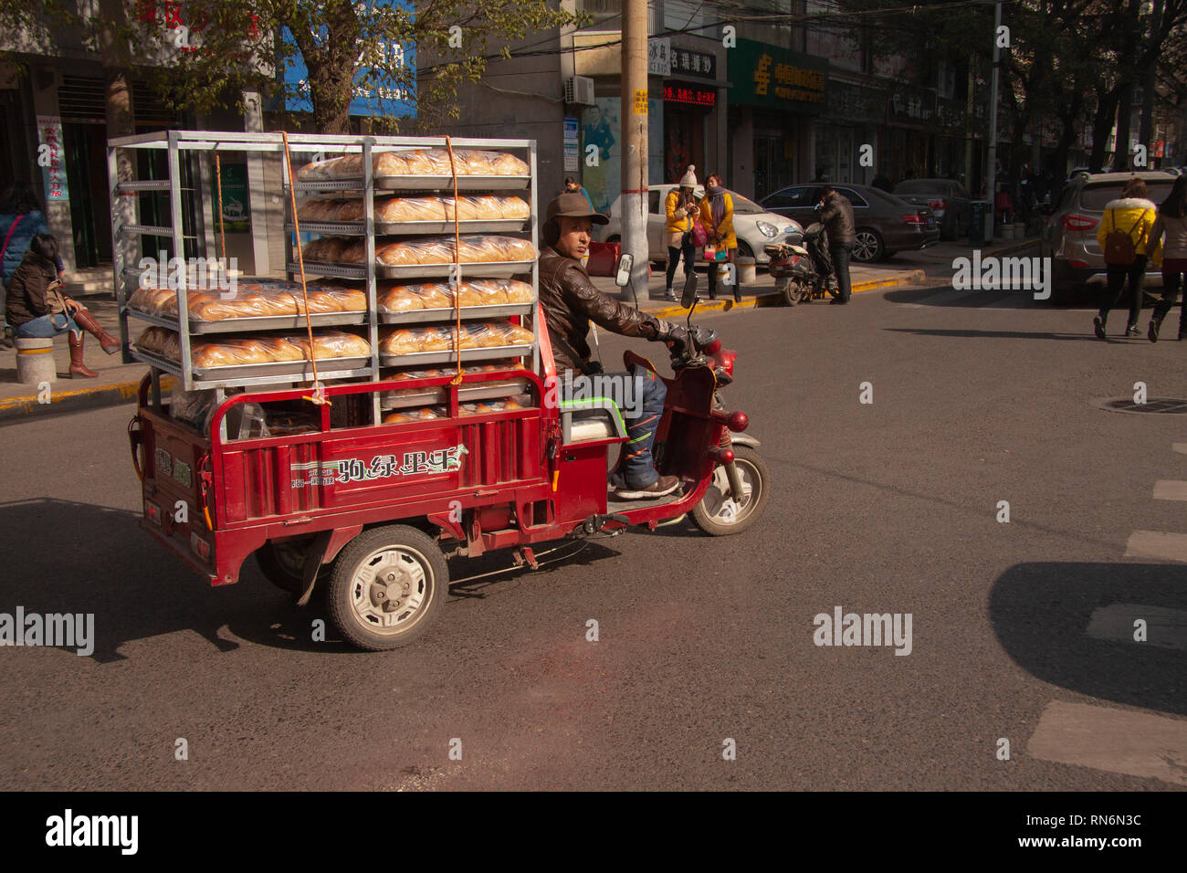 Chinese man riding a cargo moped loaded with bread from a baker in a street in China. Cargo bikes or freight mopeds are popular transport in China. Be Stock Photo