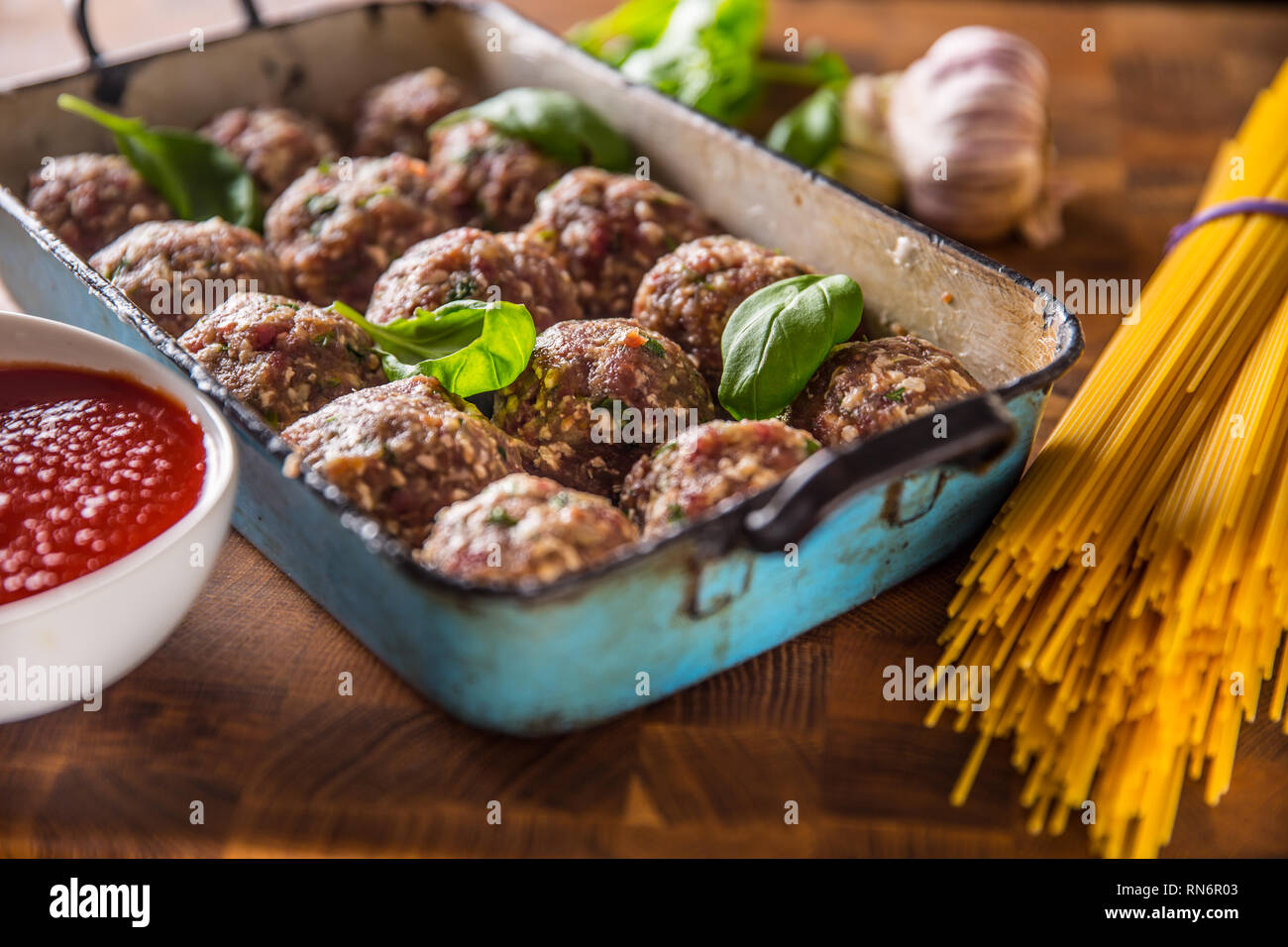 Raw feef meat balls basil tomato sauce garlic and spaghetti on butcher board. Stock Photo