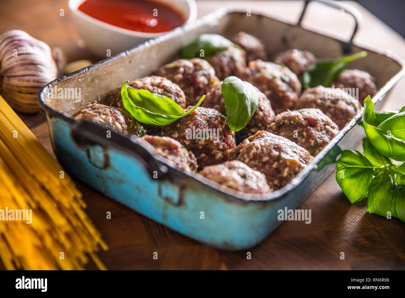 Raw feef meat balls basil tomato sauce garlic and spaghetti on butcher board. Stock Photo