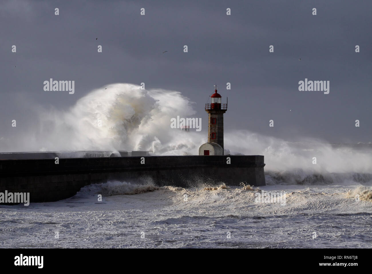 Dark storm. River mouth piers and lighthouses covered by big sea waves against an overcast sky before rain. Stock Photo