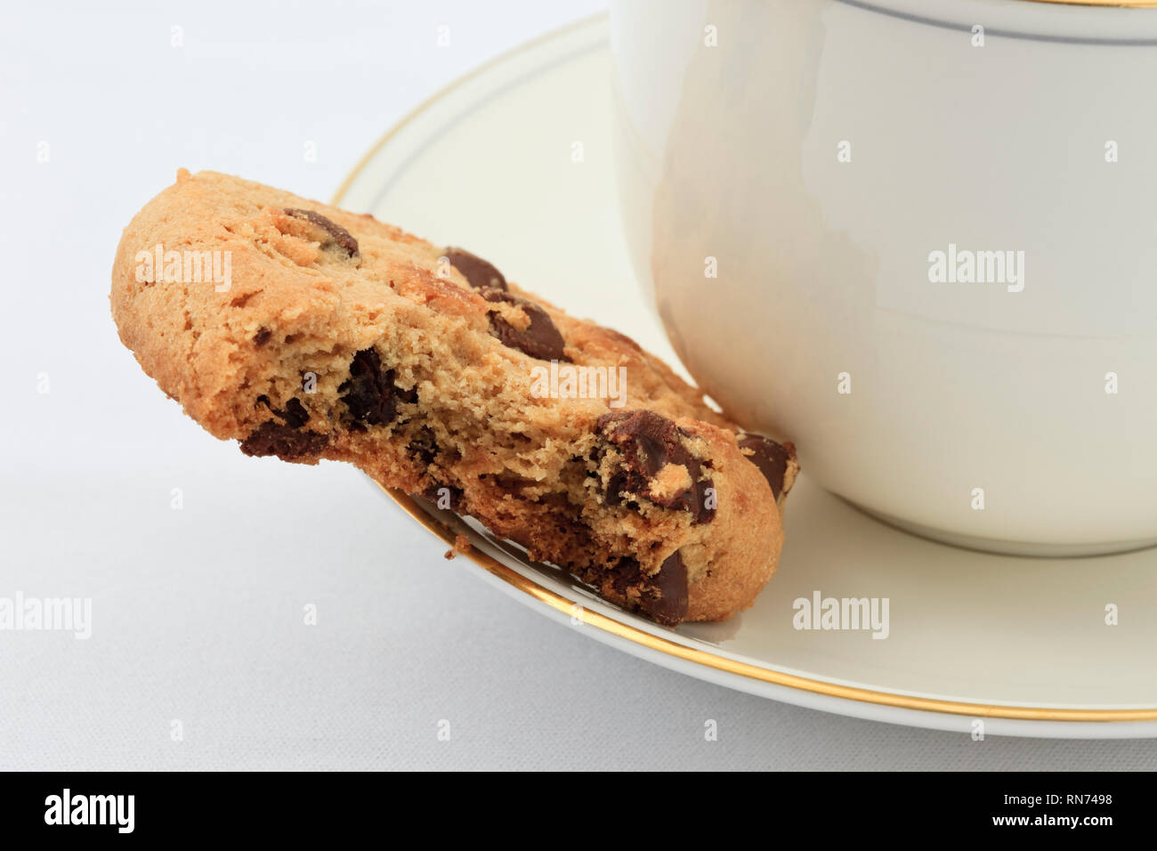 Cup of English tea on a saucer and a chocolate chip biscuit with a bite taken out. England UK Britain Stock Photo