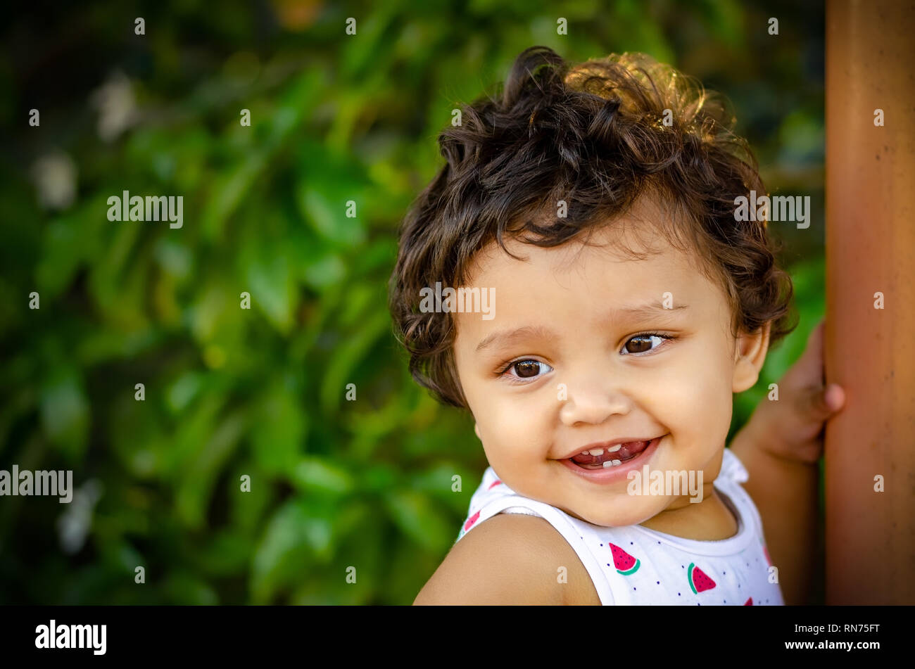 Closeup portrait of a happy Indian girl in the park with green background. Stock Photo