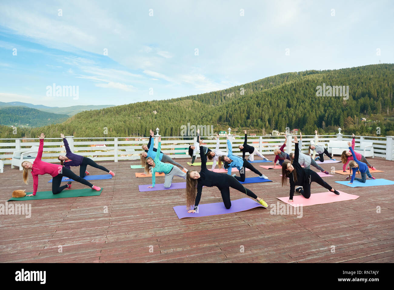 Group of sportive women doing yoga together outside on fresh air. People standing in revolved side angle pose on yoga mats, doing exercises, practicing balance. Stock Photo