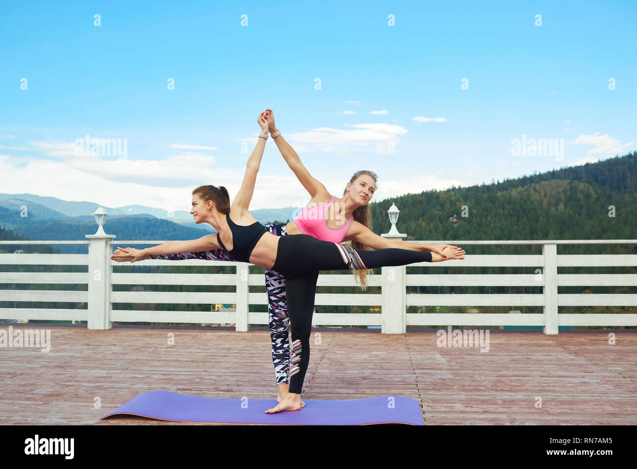 Charming Women Standing In Half Moon Pose Holding Hands Together