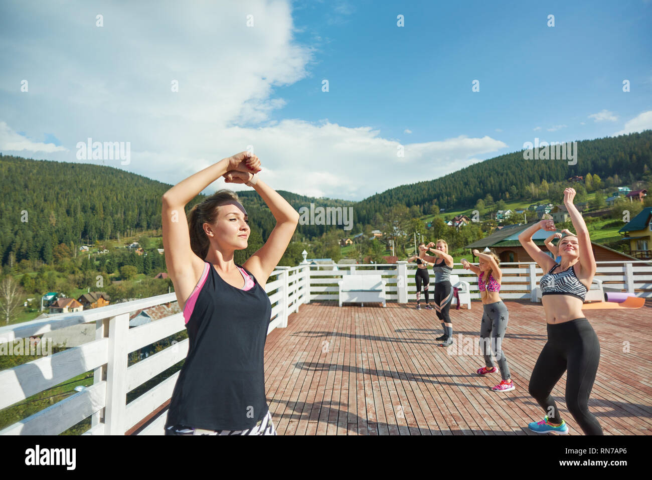 Sportive group of women repeating moves of fitness coach. Professinal fitness trainer showing exercises and practicing sports. Beautiful slender woman wearing in sportswear. Stock Photo