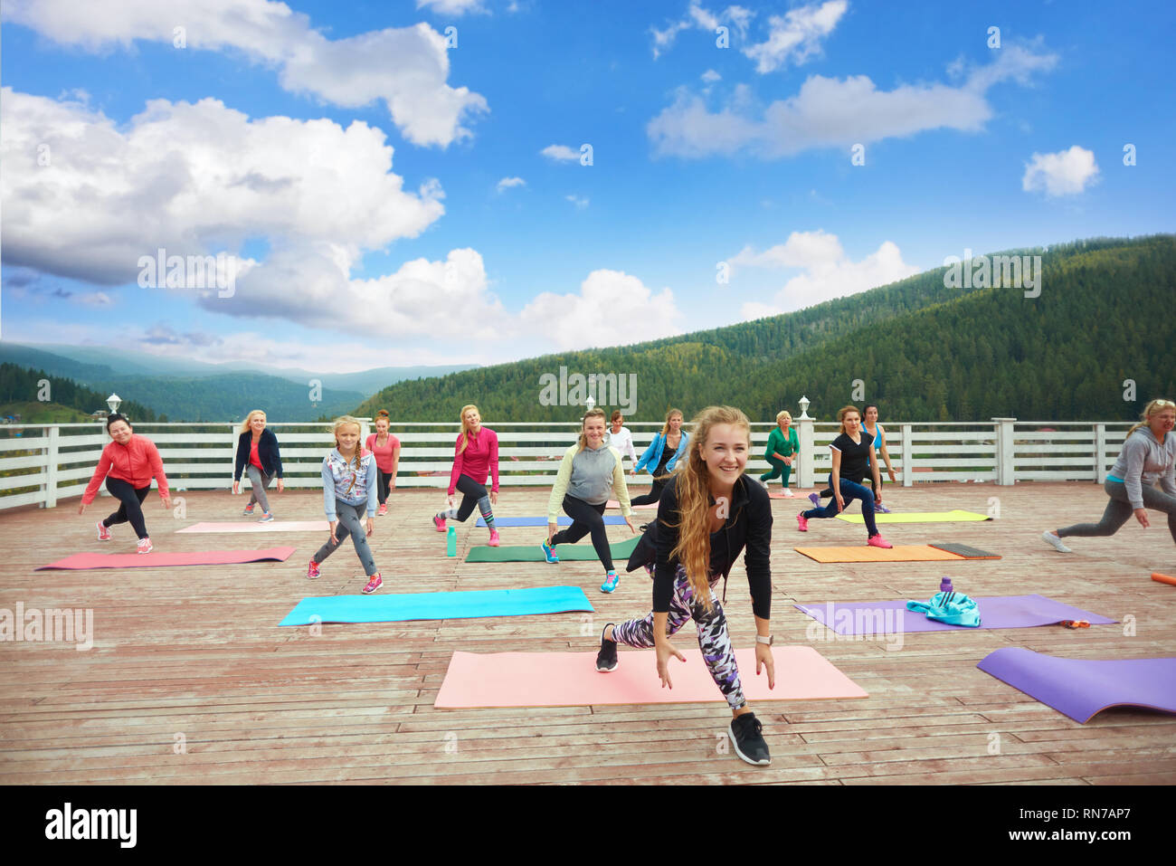 Sportive and healthy woman and girls practicing fitness during class on fresh air outside. Woman wearing in trendy sportswear. Female coach showing exercises for physical strength. Stock Photo