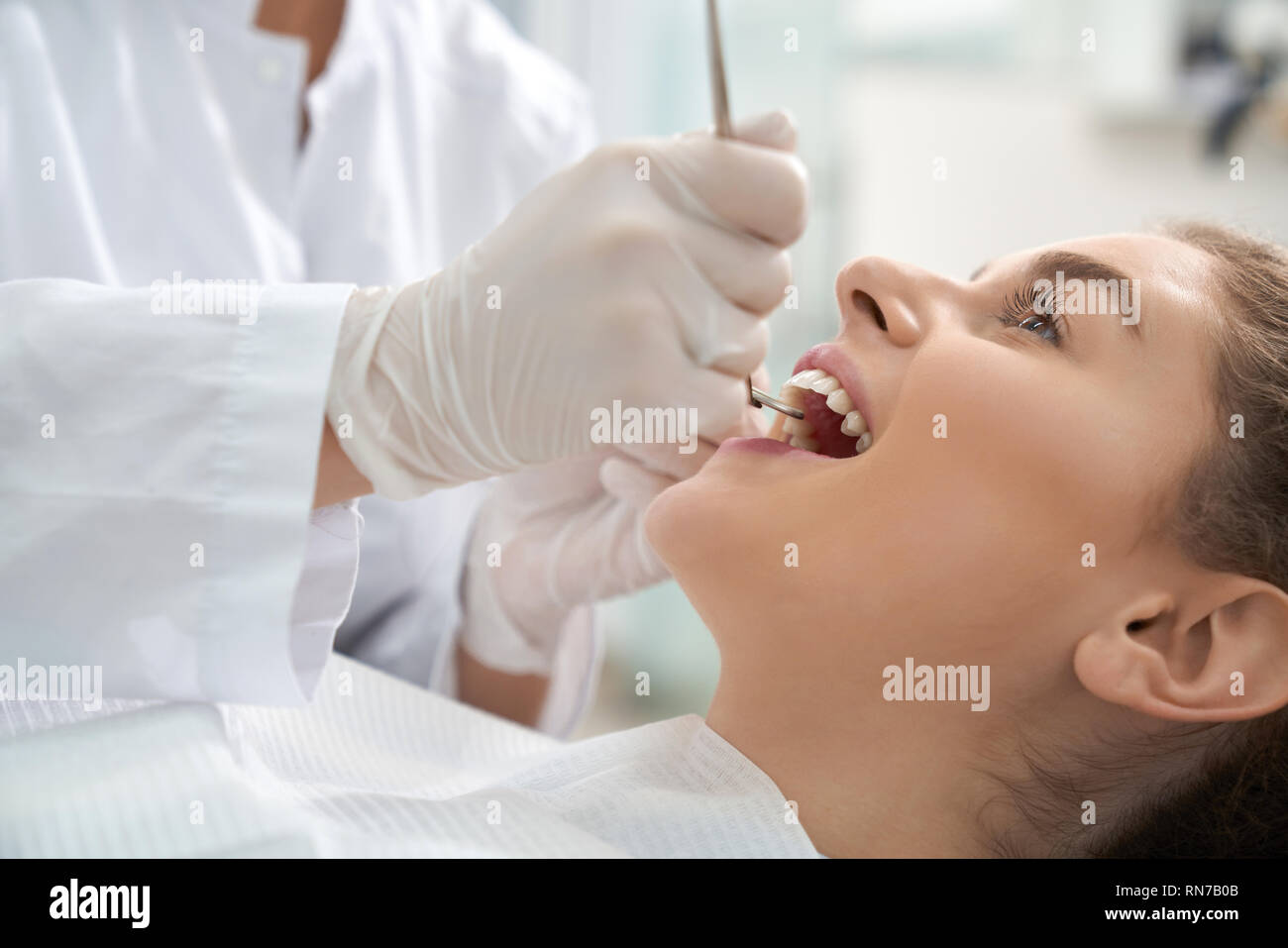 Closeup of woman lying on dental chair with open mouth and dentist in white protective gloves examining teeth. Female patient treating and caring about teeth. Concept stomatology and health. Stock Photo