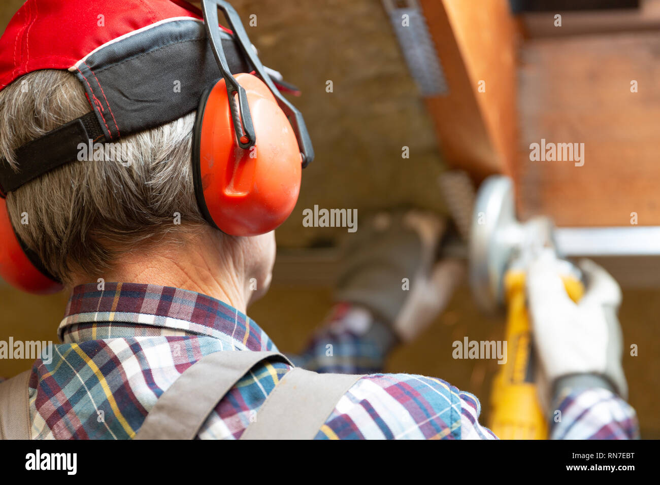 Man fixing metal frame using angle grinder on attic ceiling covered with rock wool Stock Photo