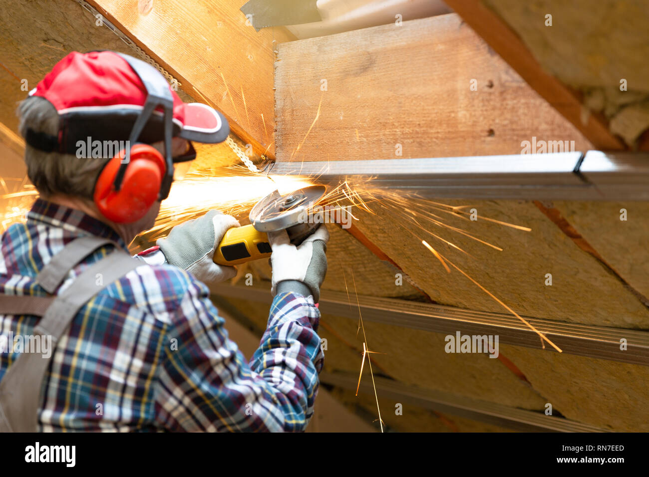Man fixing metal frame using angle grinder on attic ceiling covered with rock wool Stock Photo