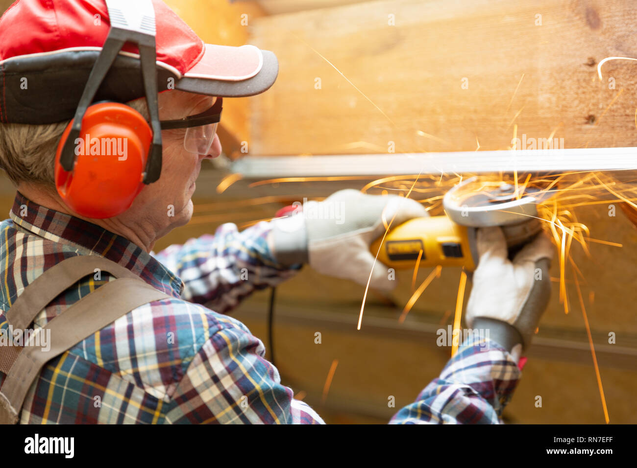 Man fixing metal frame using angle grinder on attic ceiling covered with rock wool Stock Photo