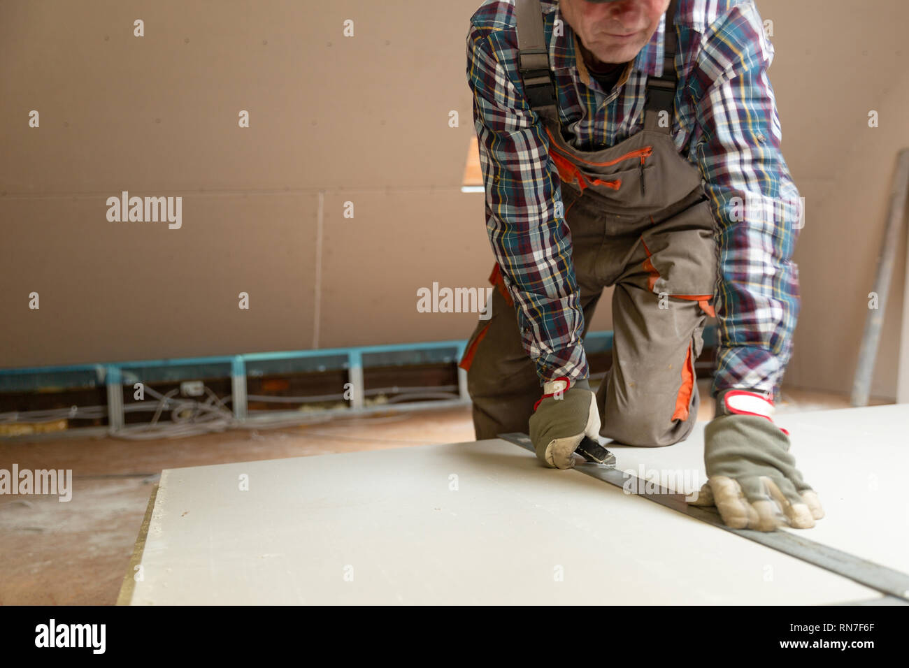 Worker cutting drywall plasterboard with construction knife. Attic