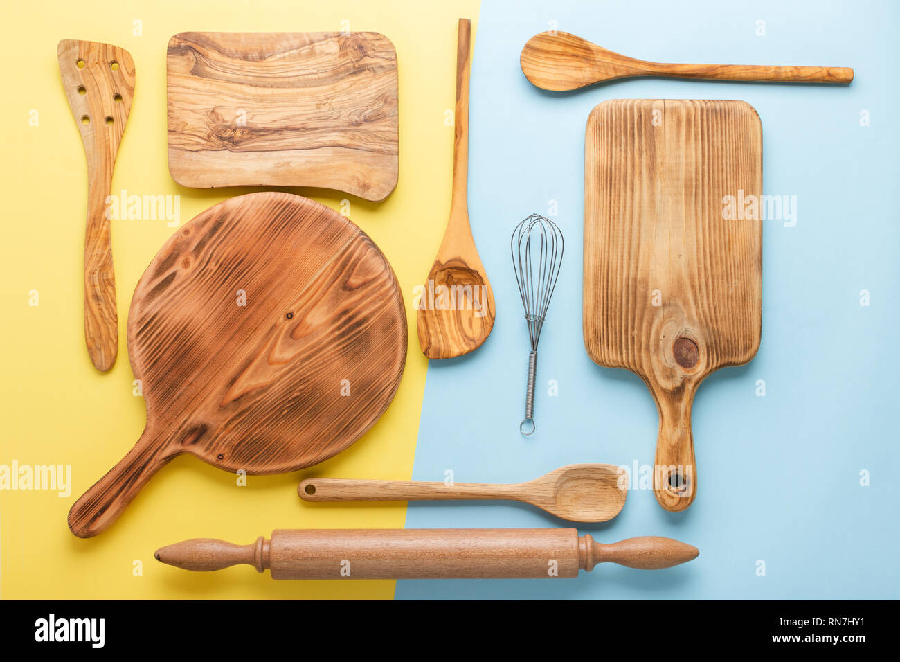 Kitchen utensils, food preparation cooking accessorises, chopping boards, wooden spoons, whisk on blue and yellow table, top view, selective focus Stock Photo