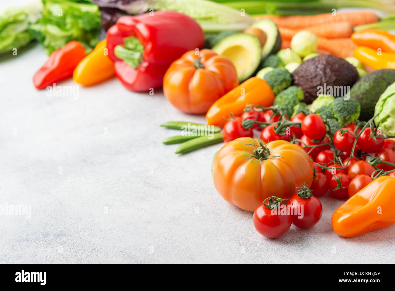 Fresh raw ingredients for salad, tomatoes cucumbers lettuce pepper avocado celery spring onion broccoli peas on the white table, copy space, selective focus Stock Photo