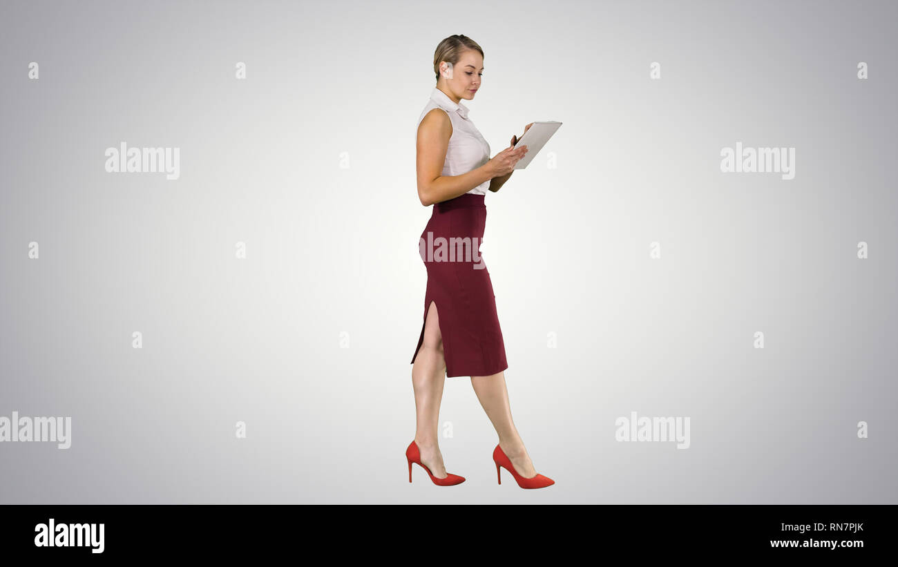 Businesswoman using electronic tab walking on gradient background. Stock Photo