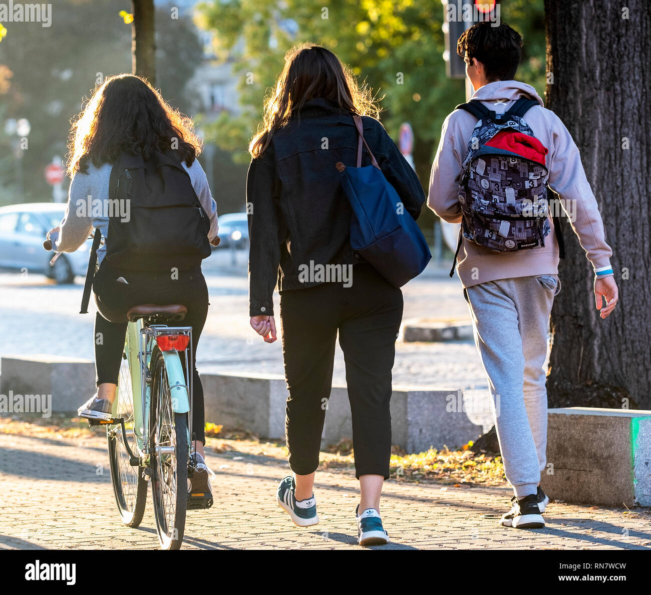 Strasbourg, Alsace, France, Europe, rear view of 2 teenagers walking and one girl biking on pavement, Stock Photo