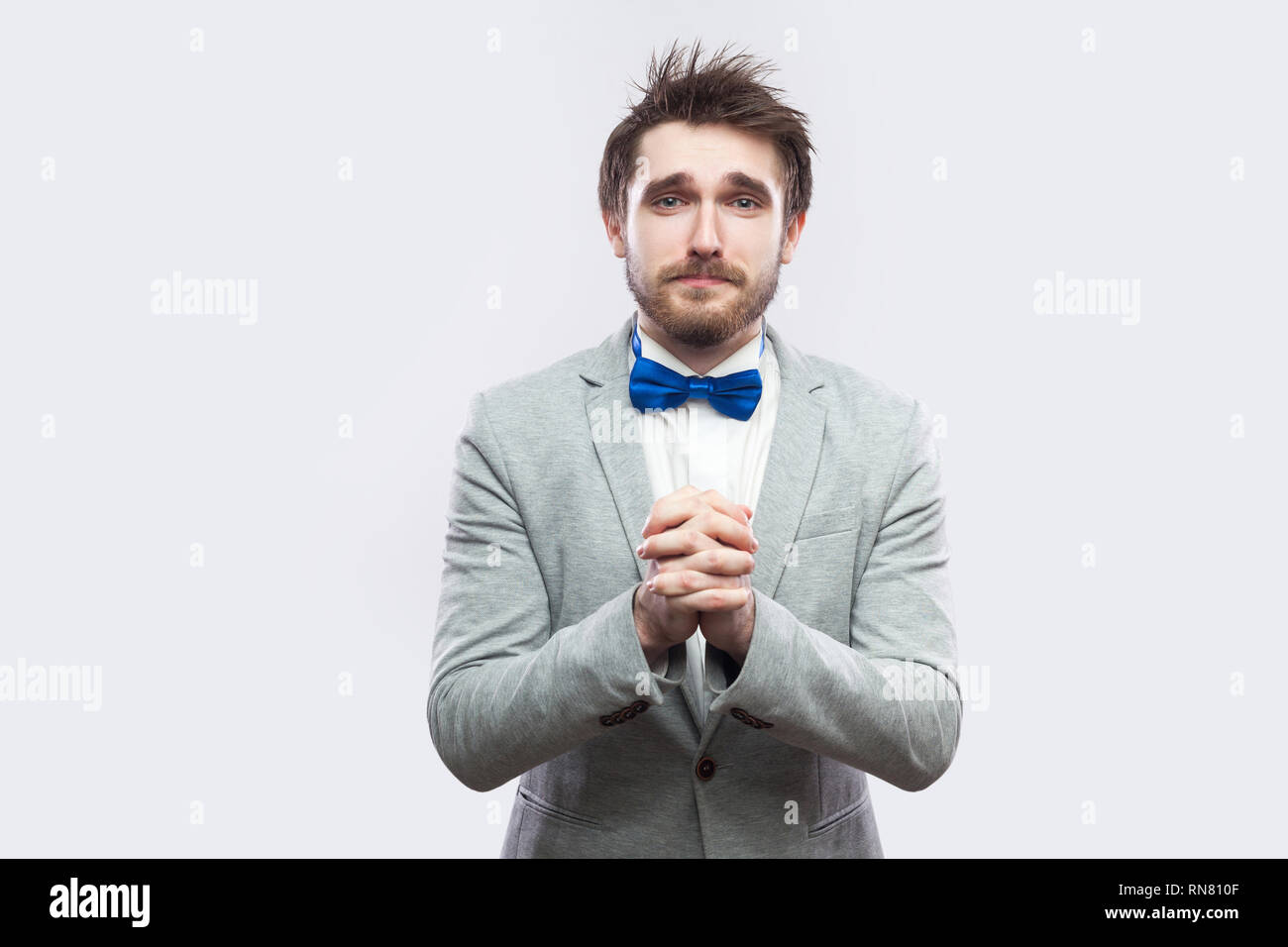 I am sorry, please forgive me. sad handsome bearded man in casual grey suit and blue bow tie looking at camera and asking for help or forgivness. indo Stock Photo