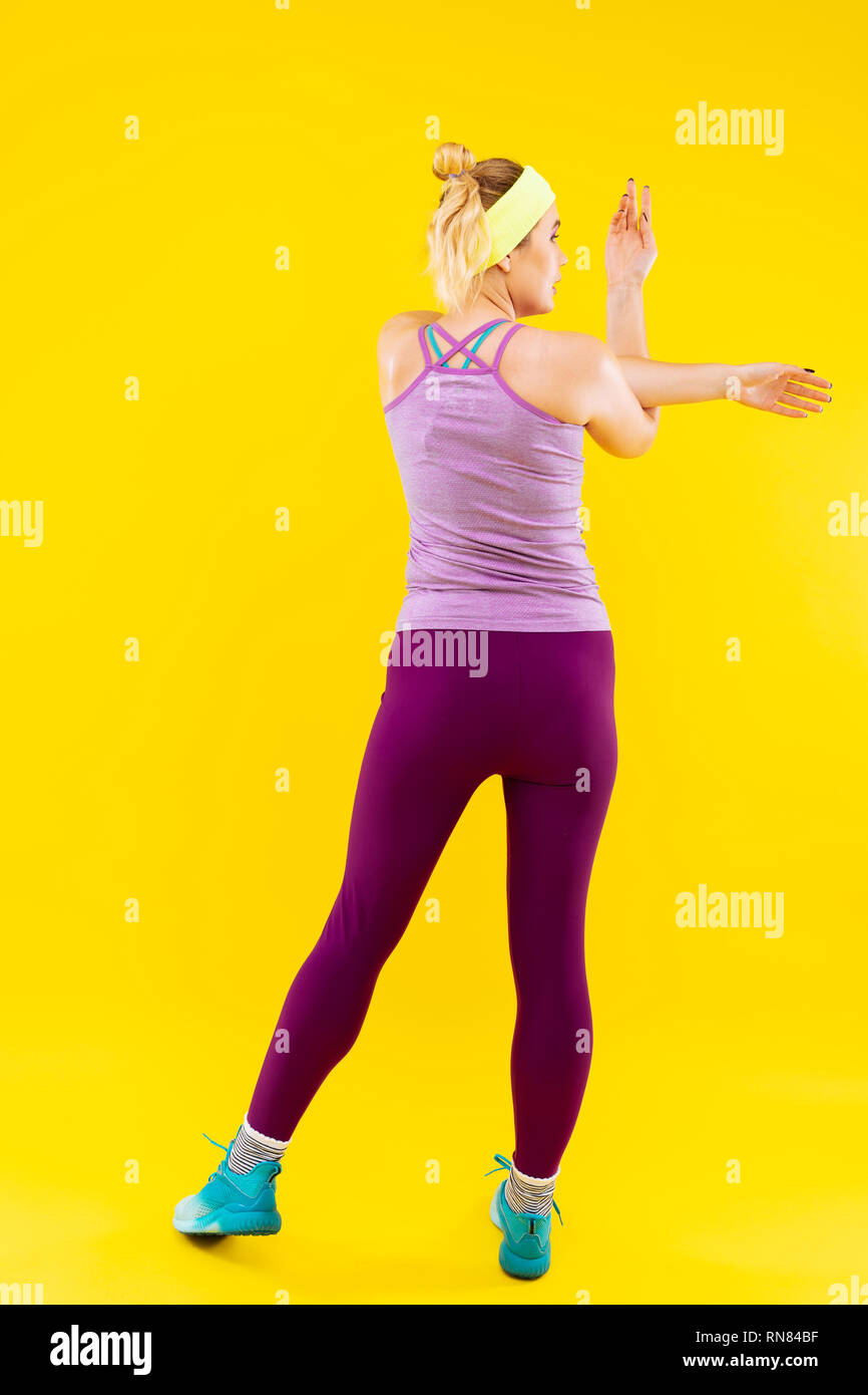 Slim woman wearing purple leggings stretching her arms Stock Photo