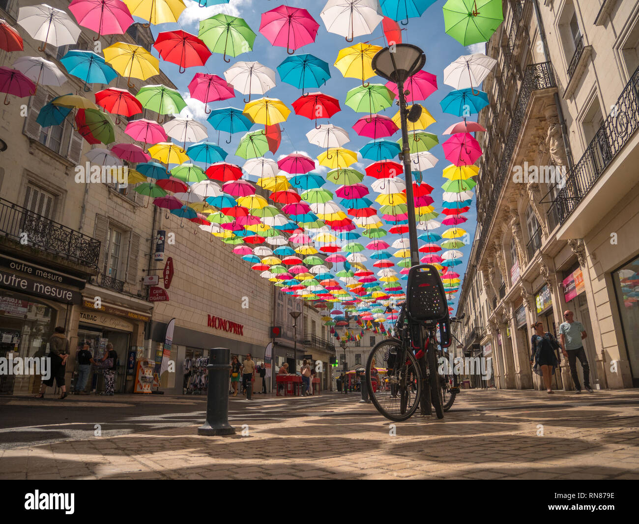 Mult-coloured rainbow umbrellas hanging over a street, with lamposts and bikes, in Saumur, Loire Valley, France Stock Photo