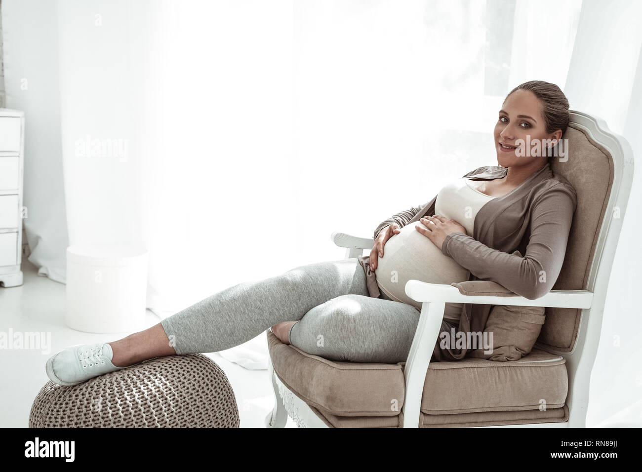 Beaming pleasant pregnant woman being relaxed while sitting Stock Photo