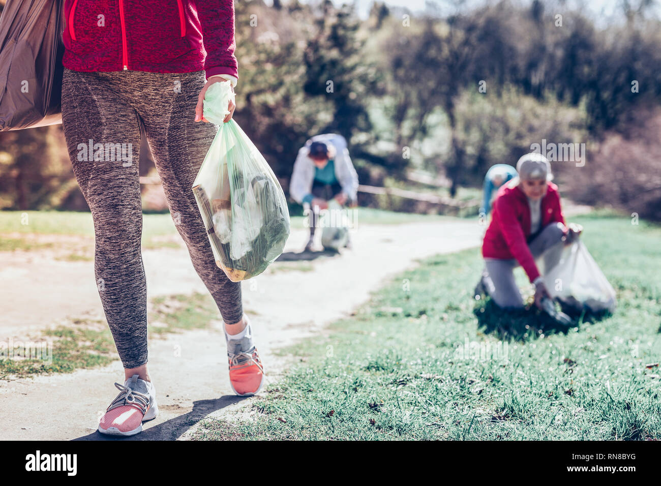 Bag with garbage. Woman wearing grey leggings and sneakers caring bag with garbage after cleaning the park Stock Photo