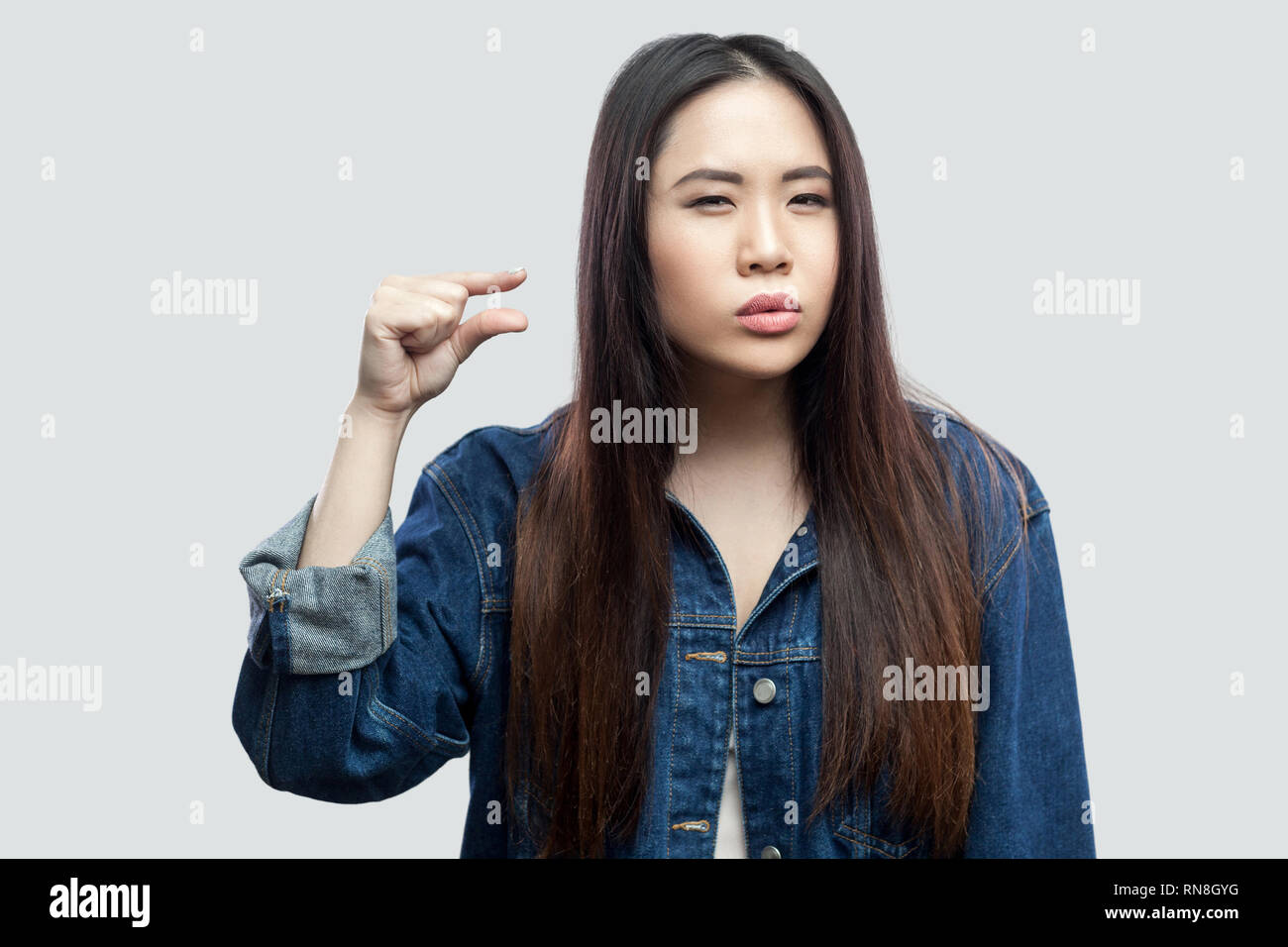 Give me few more. Portrait of beautiful brunette asian young woman in casual blue denim jacket with makeup standing and showing a little size with han Stock Photo