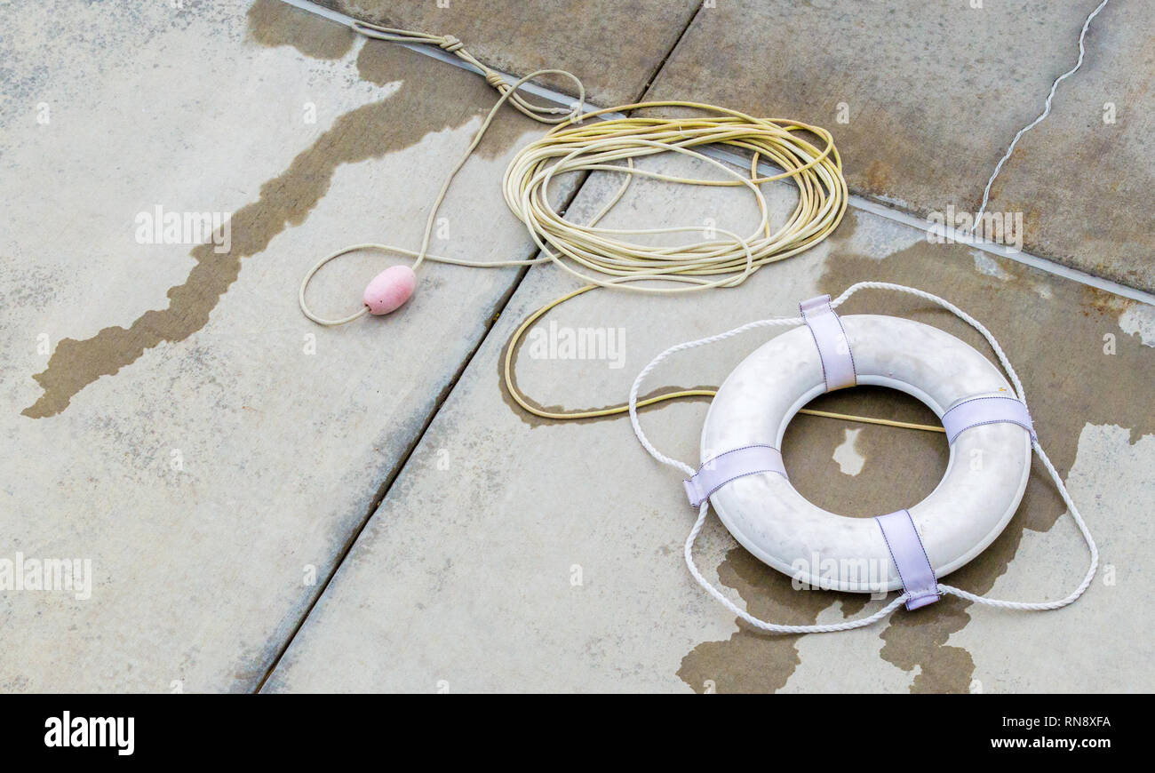 weathered ring buoy and rope on a cement pool deck with copy space Stock Photo