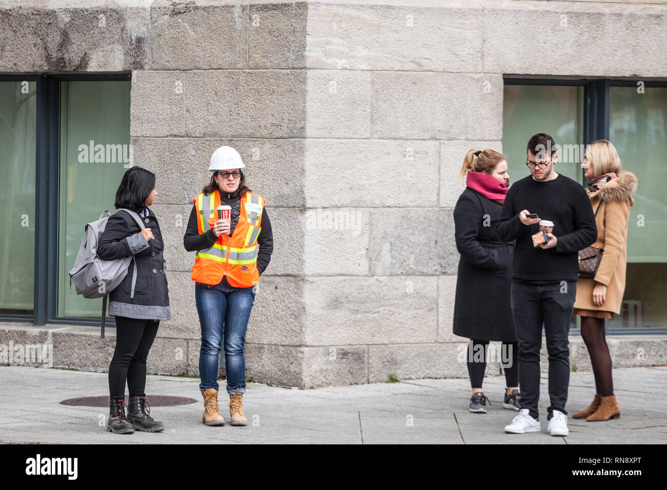 MONTREAL, CANADA - NOVEMBER 7, 2018:Young woman wearing safety PPE equipment, a helmet and an orange visibility vest discussing during her break with  Stock Photo
