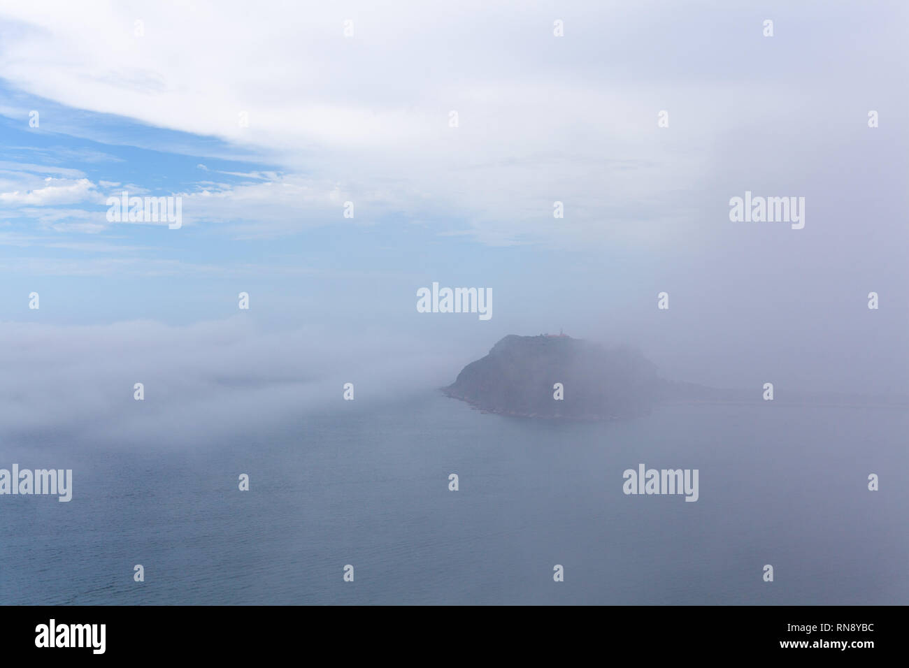 Low clouds and mist over ocean concealing a small island - mystical landscape Stock Photo