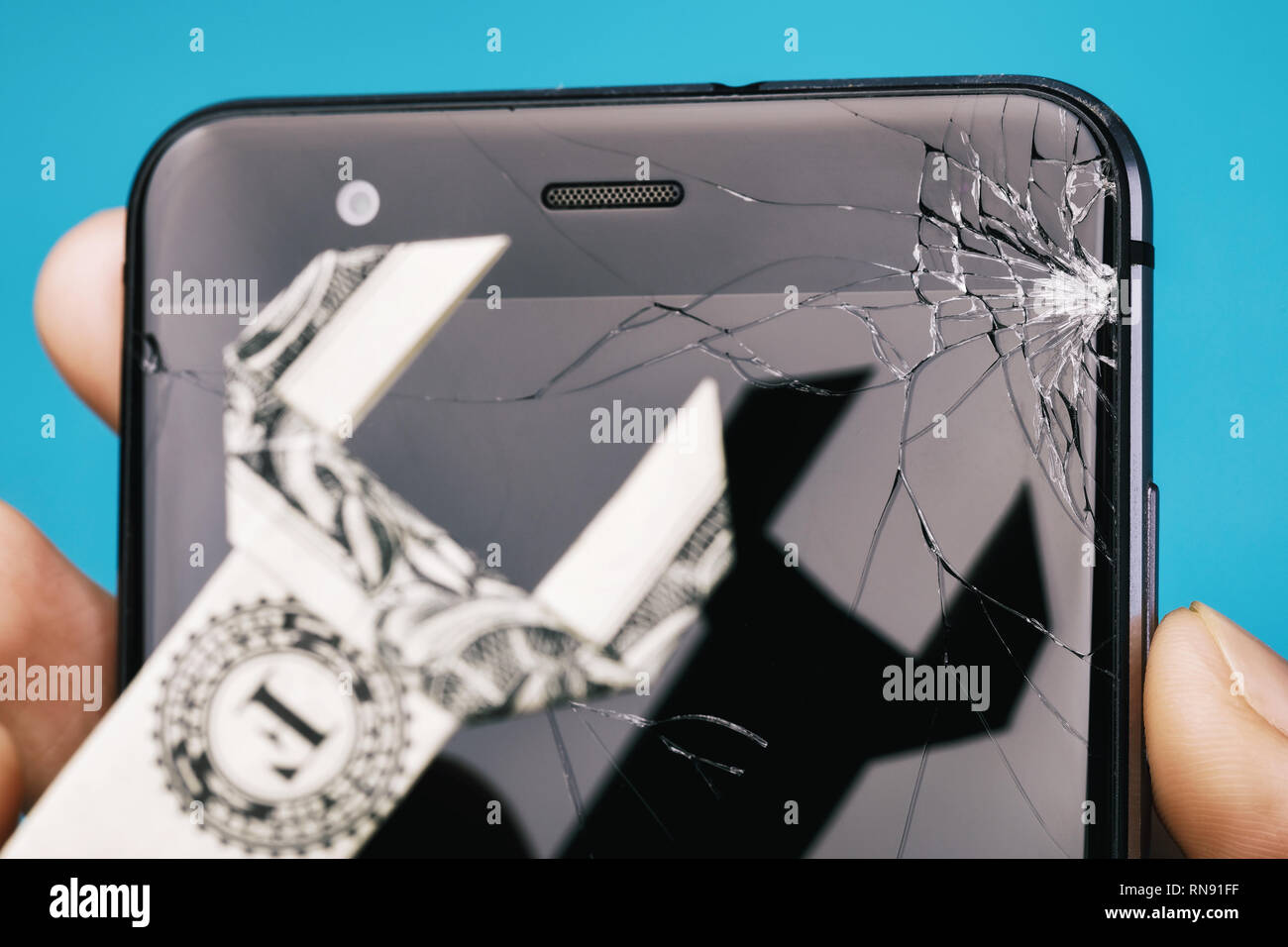 Broken screen of the phone in hand and dollar in the form of a key, as a concept on cost of repairing a mobile device, close-up Stock Photo