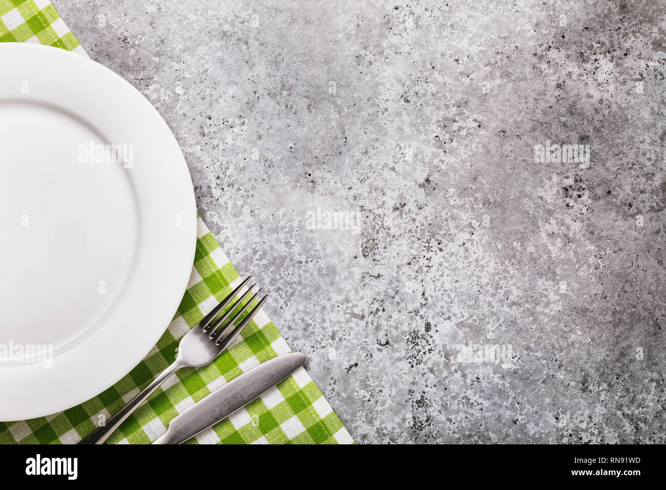 Fork, knife and white ceramic plate on the table with a concrete ...
